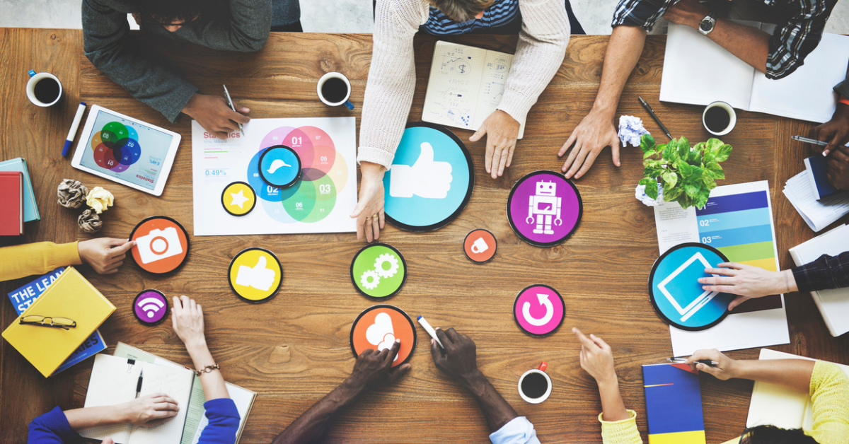 Overhead view of a team collaborating around a table with colorful social media and technology icons