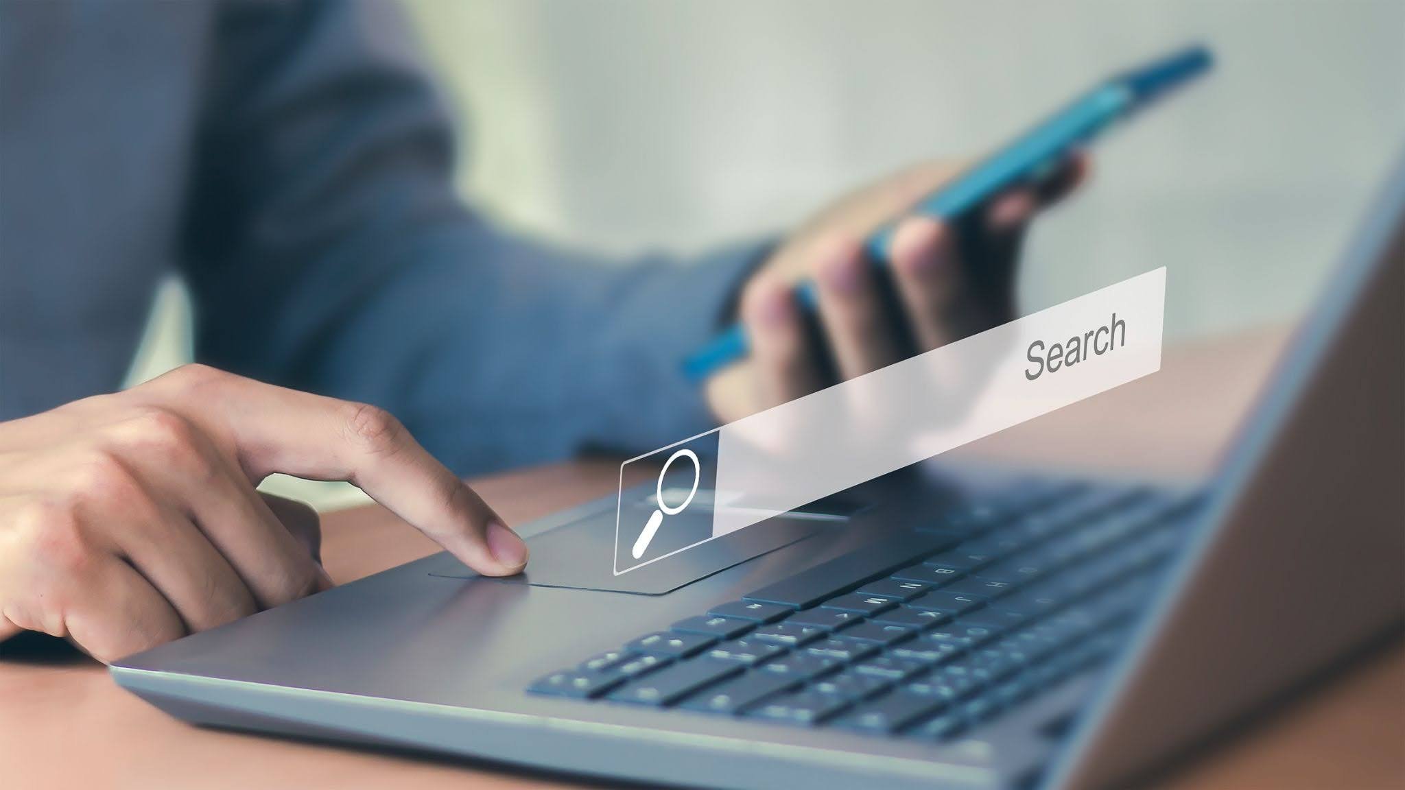 Person using a laptop and smartphone with a digital search bar overlay, representing online search or web browsing